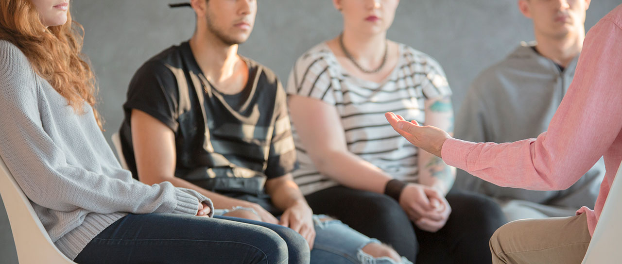 Eine Gruppe junger Erwachsener sitzt mit einer Therapeutin im Kreis.