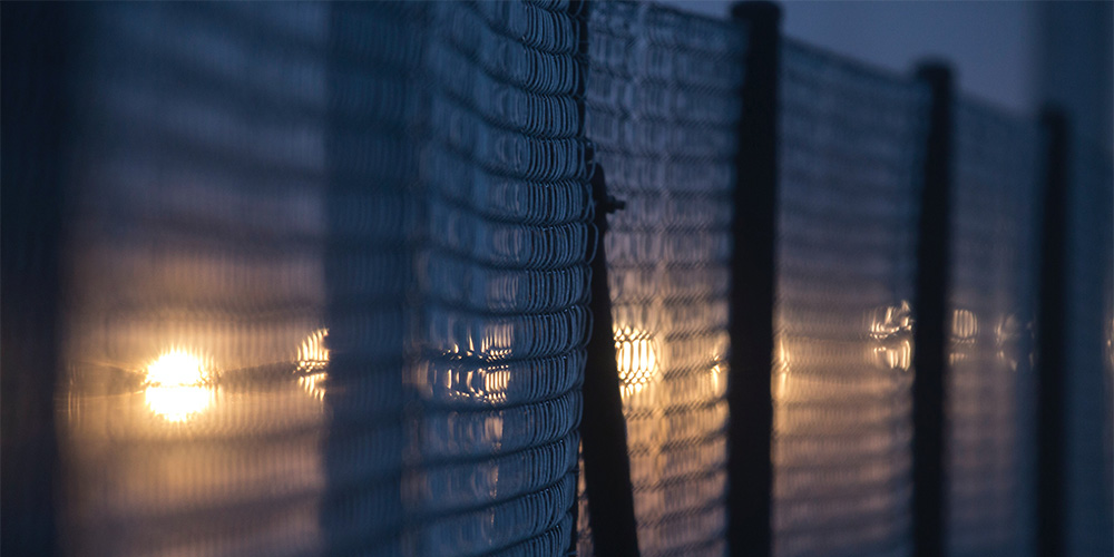 A high fence at night illuminated by spotlights A high fence at night illuminated by spotlights