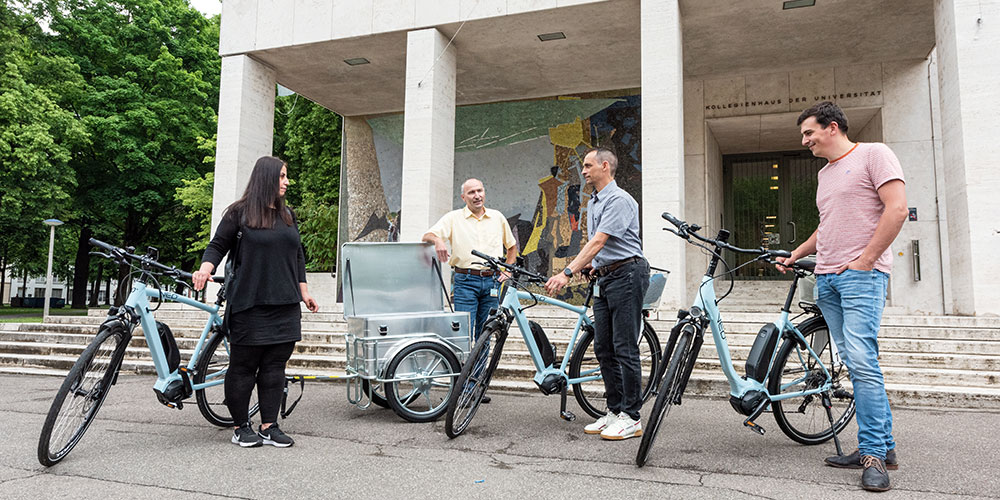 Several people with e-bikes and a bike trailer in front of the entrance to the Kollegienhaus Several people with e-bikes and a bike trailer in front of the entrance to the Kollegienhaus
