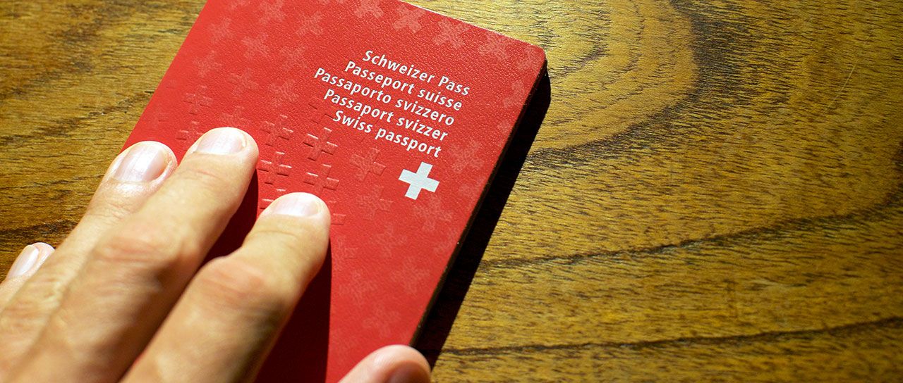 A hand resting on a red Swiss passport placed on a wooden surface.