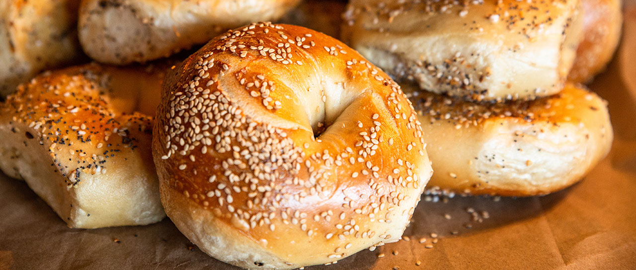 Several New York style bagels with sesame seeds lie in a heap on a sheet of baking paper.